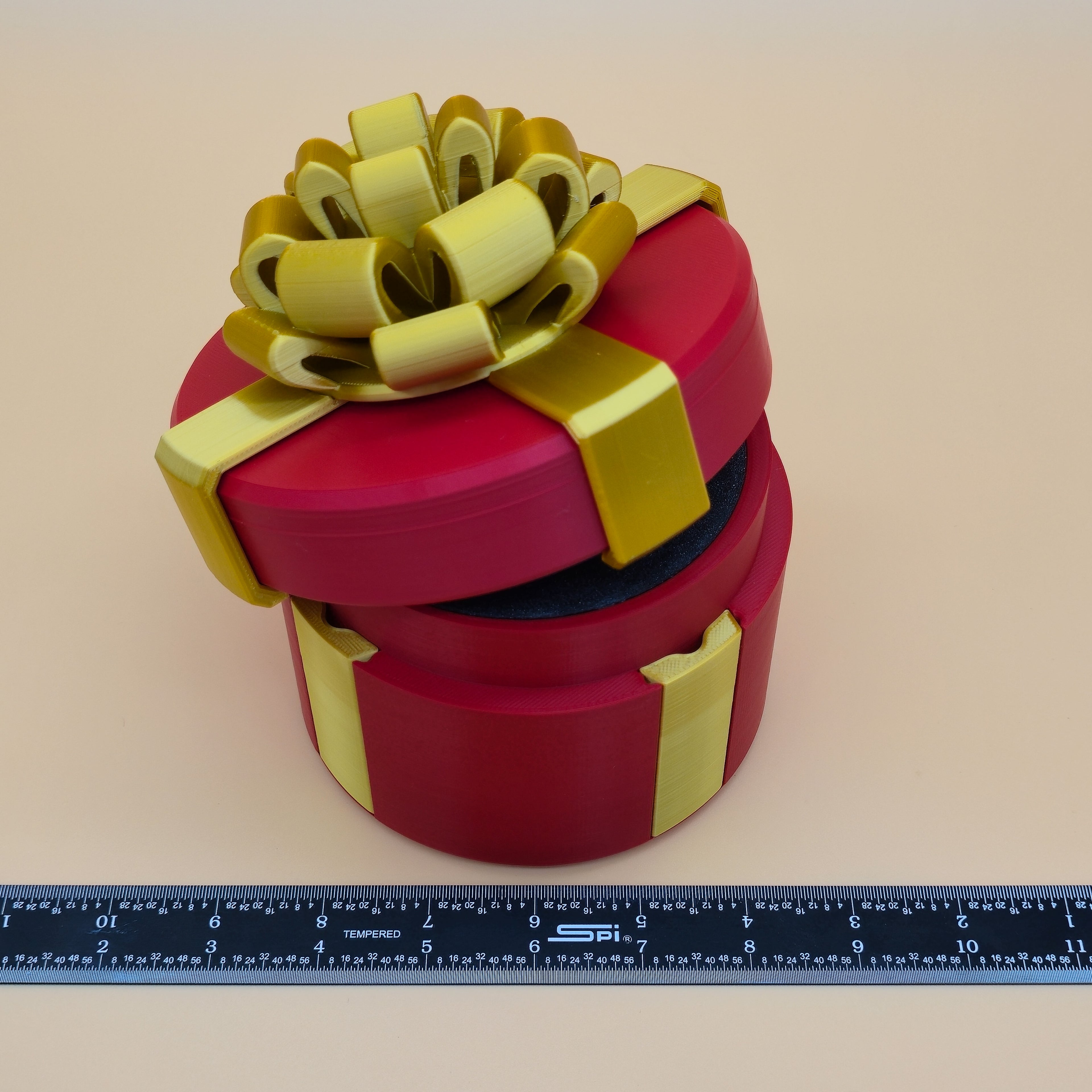 Red gift box with a gold bow on a beige background, accompanied by a ruler for scale.